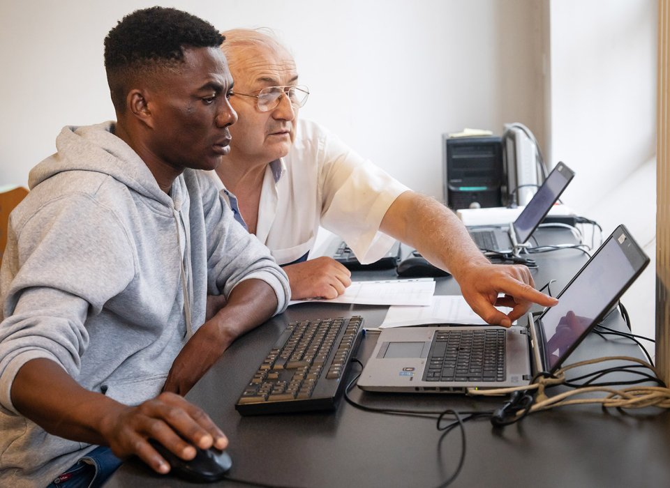 Un bénévole accompagne un jeune homme dans l'utilisation d'un ordinateur